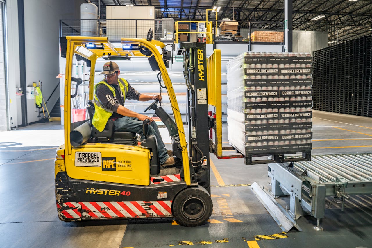 Home A warehouse worker maneuvers a forklift to transport crates for brewing company storage.