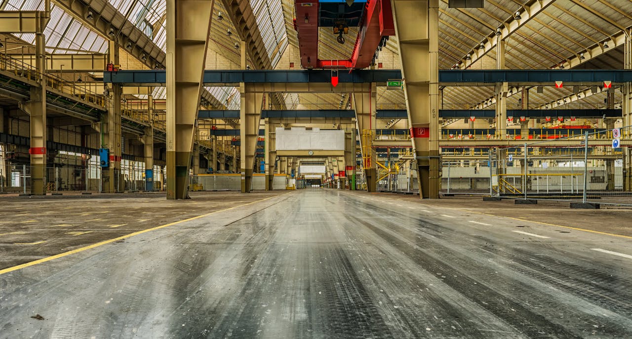 Home Wide view of an empty industrial warehouse with visible cranes and metal structures.