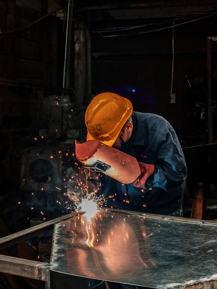 Home A welder wearing protective gear works on metal in an industrial workshop, surrounded by sparks.